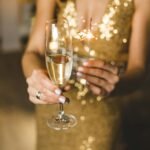 Mujer celebrando con una copa de licor, luces de bengala y vestido color dorado