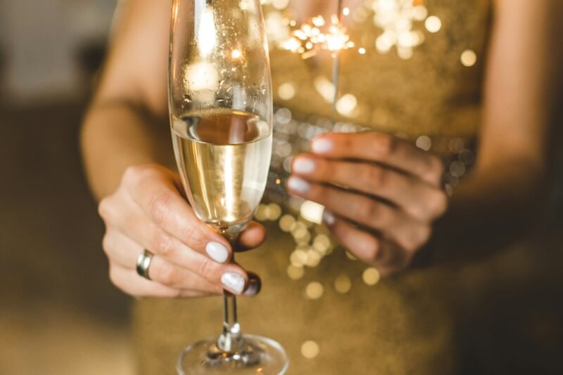 Mujer celebrando con una copa de licor, luces de bengala y vestido color dorado